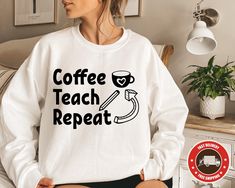 a woman sitting on a bed wearing a sweatshirt that says coffee teach repeat