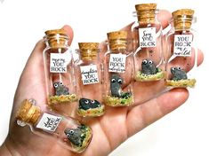 a hand holding six miniature bottles with tiny animals in them, each filled with sand