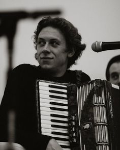 a man is playing an accordion in front of a microphone and another person behind him