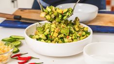 a white bowl filled with vegetables on top of a table next to bowls and spoons