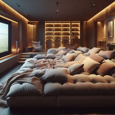 a large couch with many pillows on it in front of a television screen and bookshelves