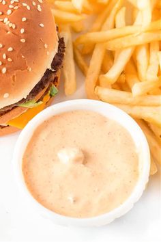 a hamburger and french fries on a white plate with a small bowl of dipping sauce