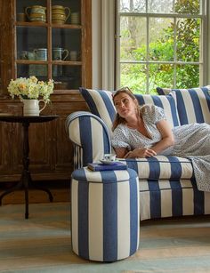 a woman laying on top of a blue and white striped couch next to a window