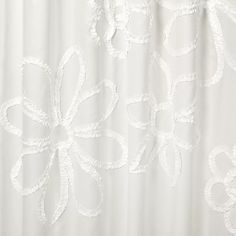 a white shower curtain with an embroidered flower design on the bottom and side panels, hanging from a metal rod