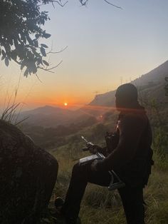 a man sitting on top of a rock next to a tree