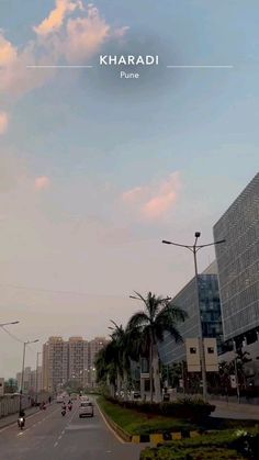 a city street with tall buildings and palm trees on both sides in front of a cloudy blue sky