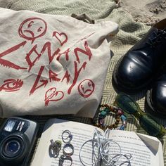 an open book, camera, sunglasses and other items are laying on the ground next to a pair of shoes