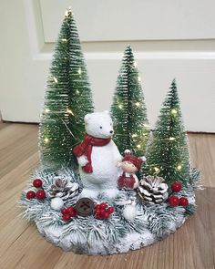 a white teddy bear sitting on top of a table next to pine cones and christmas trees