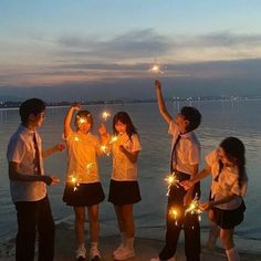 four girls and two boys holding sparklers in front of the water at night time