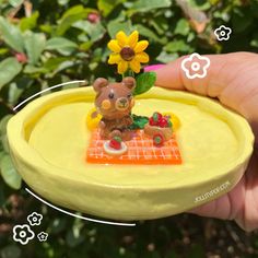 a small toy bear sitting on top of a yellow plate with flowers in the background