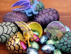 an assortment of painted eggs with dragon figurines in them on a wooden table