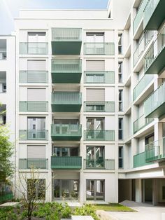 an apartment building with several balconies and plants in the foreground, on a sunny day