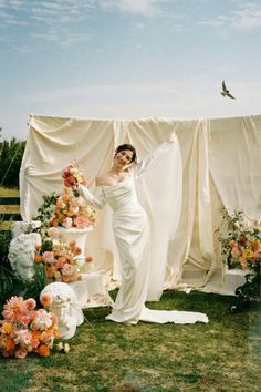 a woman standing next to a cake on top of a lush green field covered in flowers