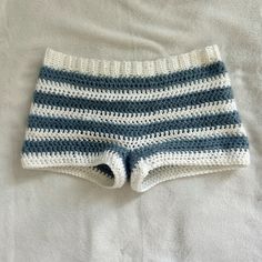 a crocheted blue and white striped shorts laying on top of a bed next to a pillow