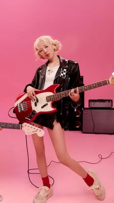 a woman with blonde hair is holding a guitar and posing in front of a pink background