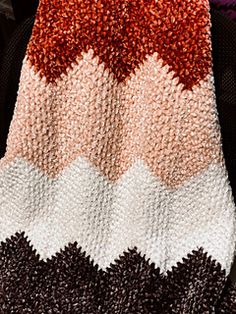 a crocheted blanket with an orange, white and black design on the bottom