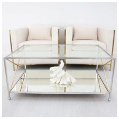 a glass coffee table with two couches in the back and white cushions on top