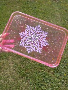 a person holding up a pink and purple tray with a flower painted on the side