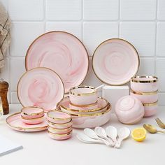 pink and gold dinnerware set on white countertop next to yellow utensils