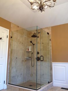 a walk in shower sitting inside of a bathroom next to a toilet and sink under a chandelier