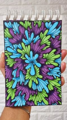 a hand holding up a spiral notebook with an image of blue and green flowers on it