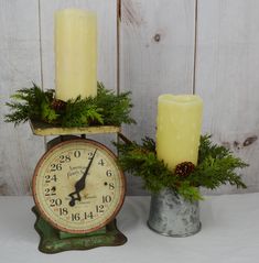 two candles are sitting next to an old clock with evergreen sprigs on it