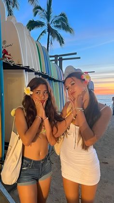 two young women standing next to each other on a beach near the ocean and surfboards