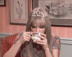 a woman wearing a tiara is drinking from a coffee cup in front of her face