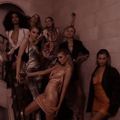 a group of women standing next to each other in front of a wall and stairs