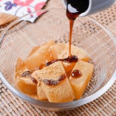 someone pouring syrup on some food in a glass bowl