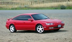 a red sports car parked in the middle of a dirt lot next to a road