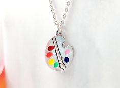 "This colorful painter's necklace is made with an antiqued silver paint palette pendant which we hand-enameled with rainbow colors and, of course, a little pink. The paint palette charm hangs on an 18-inch rhodium cable chain and makes a great gift for artists, watercolor or oil painters, art teachers or any creative person. Thank you for looking. NOTE: This listing is for one necklace with one pendant, but you can choose to purchase just the pendant without the chain (see drop down menu). The \ Artistic Hand Painted Enamel Necklaces, Artistic Silver Necklaces, Artistic Silver Enamel Necklace, Artistic Multicolor Nickel-free Necklace, Artistic Multicolor Nickel Free Necklace, Artsy Nickel-free Silver Necklace, Artsy Silver Pendant Necklace, Artsy Adjustable Silver Necklace, Artistic Adjustable Nickel-free Necklace