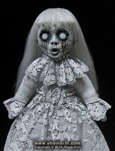 a creepy doll with white hair wearing a lace dress and headband, standing in front of a black background