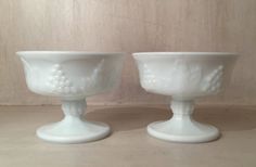 two white vases sitting next to each other on a wooden table with a wall in the background