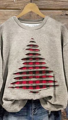 a grey sweatshirt with a red and black christmas tree on the front, hanging from a wooden hanger