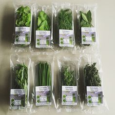 many different types of green vegetables in plastic bags on a white table with purple labels