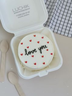 a cake in a container with the words love you written on it and spoons next to it