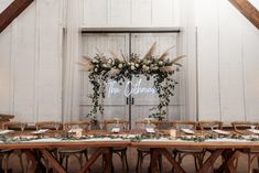 the table is set up for an event with flowers and greenery on it in front of a barn door