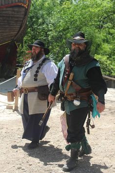 two men dressed in pirate garb standing next to each other on a dirt ground