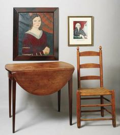 an old wooden table and chair next to a portrait on the wall in a room