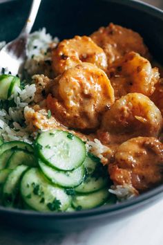 a bowl filled with rice, cucumber and meat next to a fork on top of it