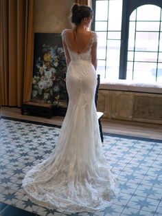 a woman standing in front of a window wearing a wedding dress with an open back