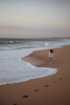 a person walking on the beach with footprints in the sand and waves coming toward them