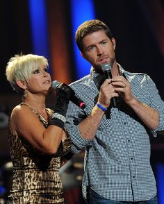 a man holding a microphone and standing next to a woman with short blonde hair on stage