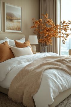 a bed with white sheets and pillows next to a vase with orange flowers in it