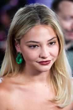 a woman with long blonde hair wearing green earrings