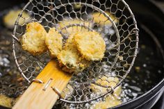 fried food being cooked in a frying pan with a wooden spatula on the side