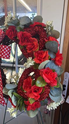 a wreath with red flowers and greenery in front of a glass door on a sunny day