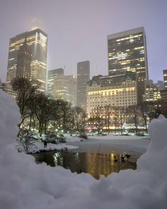 the city skyline is lit up at night with snow on the ground and buildings in the background