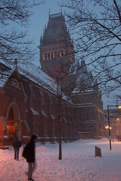 people are walking through the snow in front of an old building with a clock tower